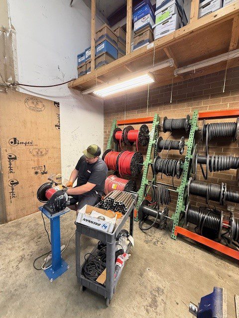 A person using a rotary machine in a workshop with shelves of coiled cables.
