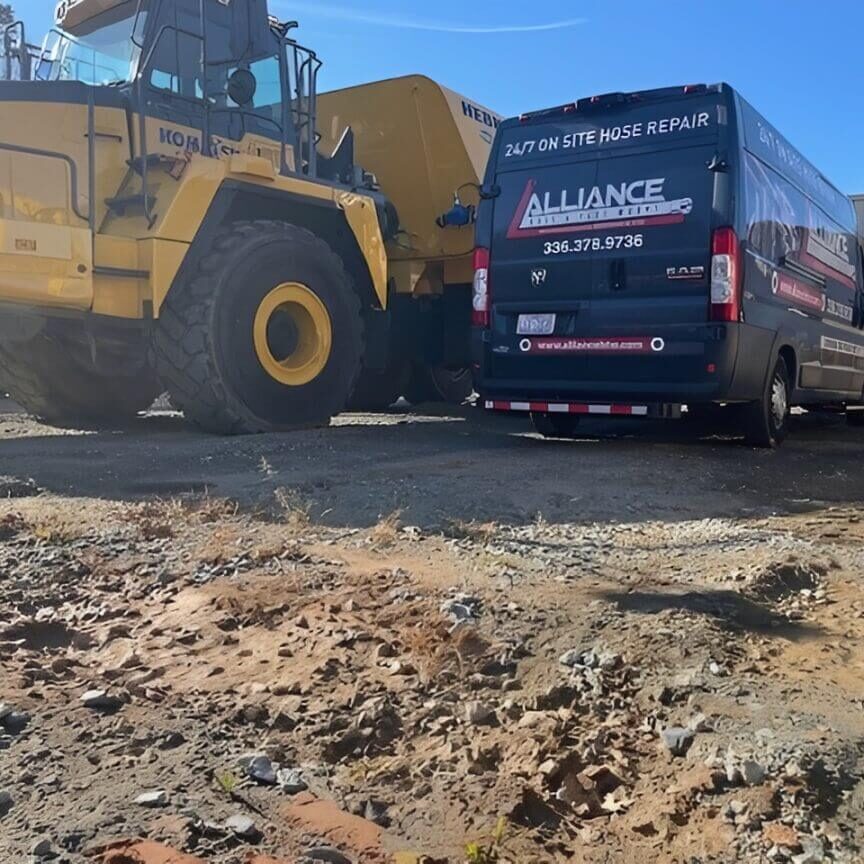 A large yellow mining truck and a black tour bus parked on a dirt road under clear blue sky.